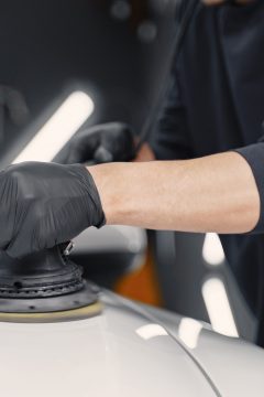 Man in a garage. Worker polish a car. Man in a black uniform.